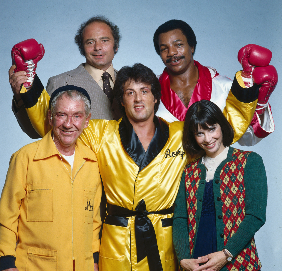 Portrait of Sylvester Stallone, as Rocky Balboa, with the cast of the "Rocky II" movie. (From left) Burgess Meredith as Mickey Goldmill, Burt Young as Paulie, Carl Weathers as Apollo Creed, and Talia Shire as Adrian. Los Angeles, California 11/1978 (Image # 1147 )